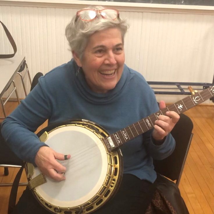 Murphy Henry sitting down and playing a gold plated archtop gibson banjo and smiling.